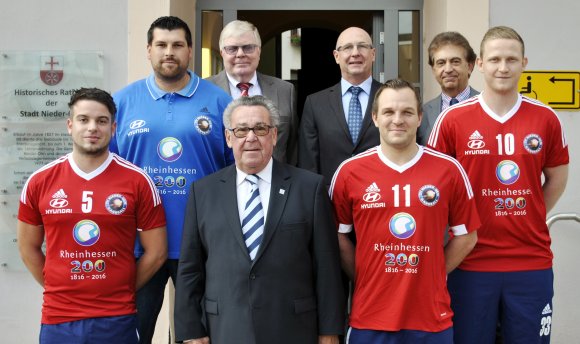 Die Handballer des TV Nieder-Olm werben auf ihren Trikots demnächst für das Rheinhessenjubiläum. Hinten von links: Trainer Markus Herberg, TV-Vorsitzender Reinhard Schmitt, Stadtbürgermeister Dieter Kuhl, Beigeordneter Franz-Josef Schatz. Vorne von links: Christopher Gaul, Peter Eugen Eckes (Vorsitzender Rheinhessen-Marketing), TV-Kapitän Tino Stumps und Lukas Berkessel.