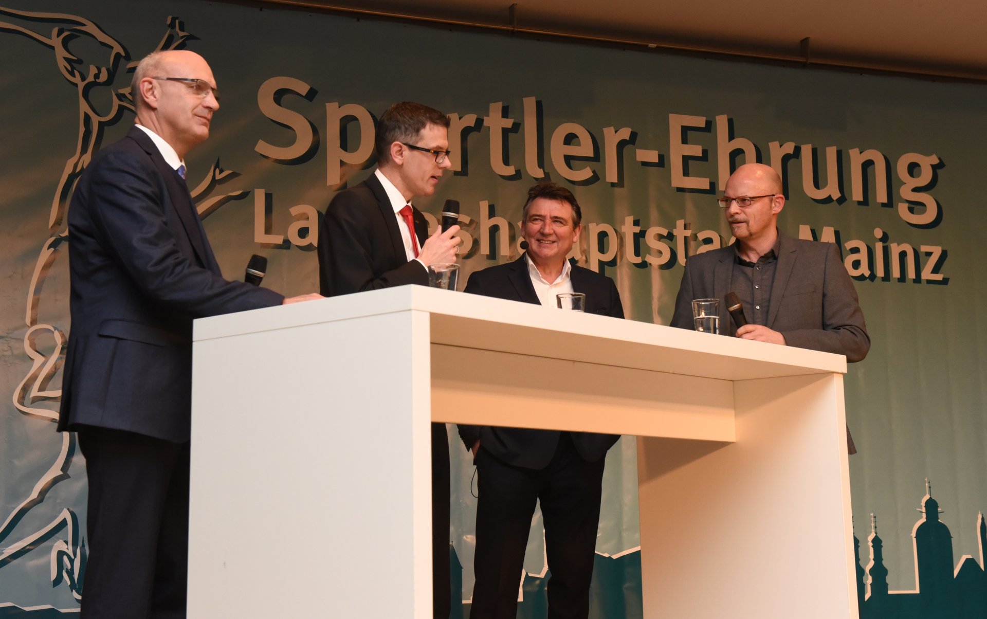 Die Mainzer Volksbank und die Mainzer Sparkasse sind seit Jahren ein verlässlicher Partner des Mainzer Sports und auch der Sportlerehrung. Die Vorstandsvorsitzenden Uwe Abel (l.) und Thorsten Mühl erläuterten die Beweggründe ihres Engagements, sagten bereits die Patenschaft für die Ehrung 2019 zu und scheinen gewillt, beim kommenden Gutenberg-Marathon eine Staffel zu bilden mit Bürgermeister Günter Beck und SPORTAUSMAINZ.de-Redakteur Peter H. Eisenhuth, der als Moderator durch den Abend führte.