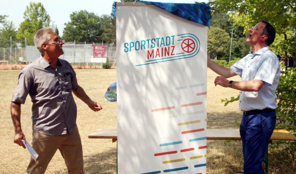 Die Enthüllung eines Gemeinsinn stiftenden Leitbegriffs: Die Vereine sollen sich als Teil einer Sportstadt Mainz verstehen, so die Hoffnung des Stadtsportverbandsvorsitzenden Alexander Reinemann (l.) und von Oberbürgermeister Michael Ebling.