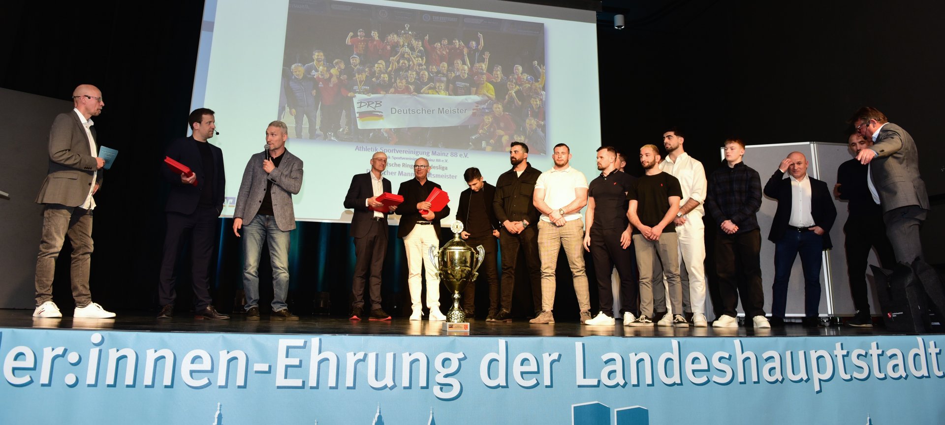 Und dann fluteten die Ringer die Bühne. Mit Ibrahim Fallacara, Ashot und Iosif Shahbazyan, Abdallh Karem, Fabian Pelzer, Wladimir Remel, Alen Tamrazow, Bachuki Gavaselishvili und Alexander Semisorow aus der Meistermannschaft, Teammanager Gianluca Natale, Betreuer Ernest Tamrazov, den Trainern Davyd Bichinashvili und Harun Yildiz sowie dem Vorsitzenden Baris Baglan…