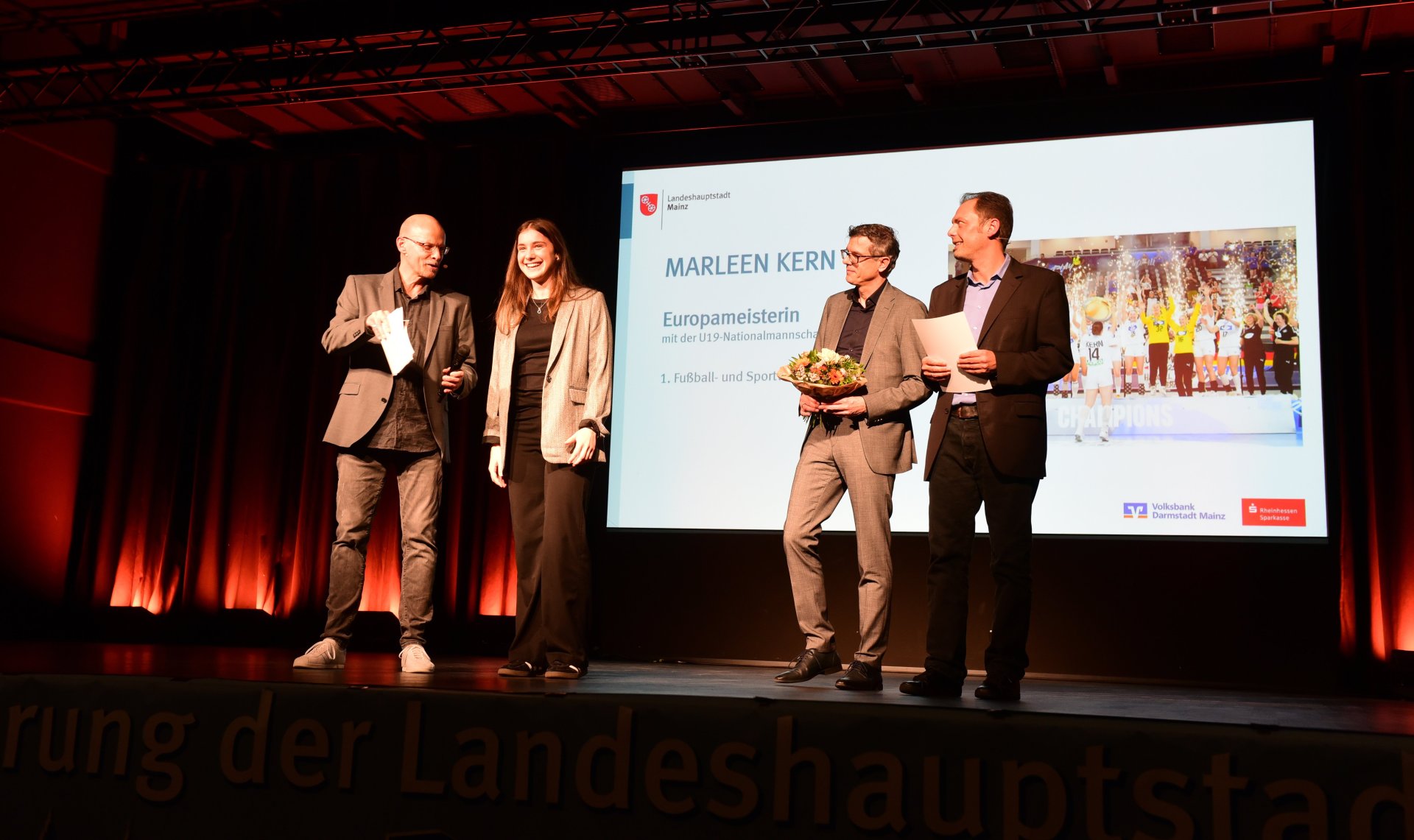Den Auftakt der Geehrten bildete Marleen Kern. Die Handballerin des FSV Mainz 05 wurde voriges Jahr Europameisterin mit der deutschen U19. Dafür gab es von Thorsten Mühl (2.v.r.), dem stellvertretenden Vorstandsvorsitzenden der Rheinhessen-Sparkasse, und dem neuen Sportdezernenten Daniel Köbler Blumen und eine Urkunde.